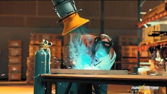 Fume extractor arm capturing welding smoke and fumes in a large industrial workspace to protect worker air quality.