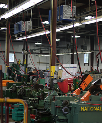 Pair of ceiling-mounted Blue Ox 3500C air cleaners filtering oil mist above cold-header machines at Mac Fasteners.